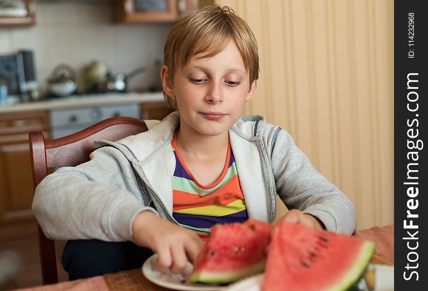 A boy sits at the table and eating watermelon. A boy sits at the table and eating watermelon