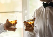 Two Glasses Of Whiskey In The Hands Of Men In White Shirts And Bow Ties. Secular Evening, Toast, Friendship Royalty Free Stock Photography