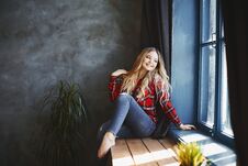 Happy And Smiling Beautiful Blonde Girl In Jeans And Red Plaid Shirt, Sits And Posing Near The Window And Looks Outside Royalty Free Stock Photos Happy And Smiling Beautiful Blonde Girl In Jeans And Red Plaid Shirt, Sits And Posing Near The Window And Looks Outside Royalty Free Stock Photos