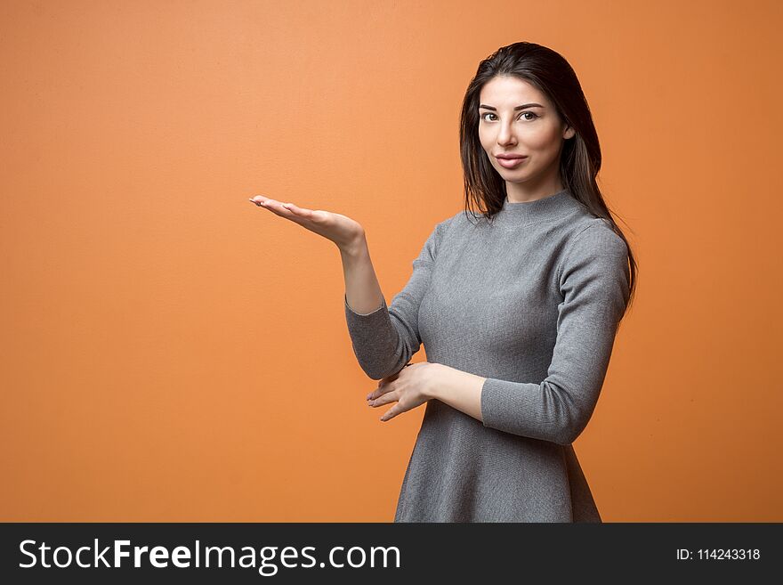 Portrait of a young beautiful business woman in neutral dress holding out empty hand and looking into camera