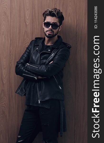 Image of a fashion side man stands with crossed hands on a wooden background. Image of a fashion side man stands with crossed hands on a wooden background