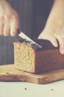 Woman Hands Slicing Freshly Backed Bread. Handmade Brown Loaf Of Bread, Bakery Concept, Homemade Food, Healthy Eating Stock Photo