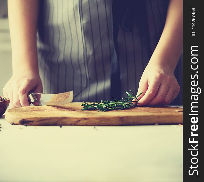 Woman hands cutting fresh green rosemary on wood chopping board in white kitchen, interior. Copy space. Homemade food conceplt, healthy recipe.
