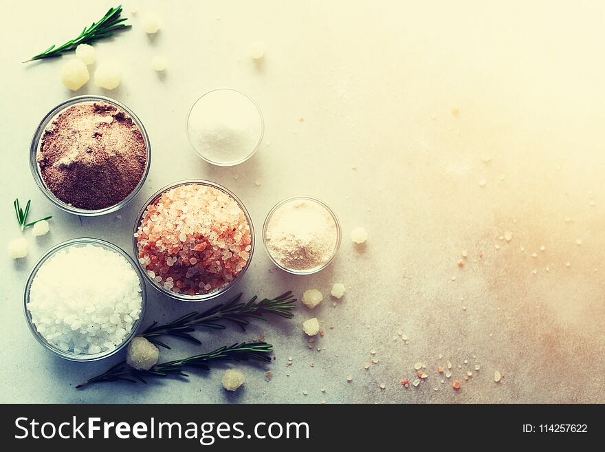 Mix of different salt types on grey concrete background. Sea salts, black and pink Himalayan salt crystals, powder, rosemary. Salt crystal balls from Dead sea. Copy space. Top view