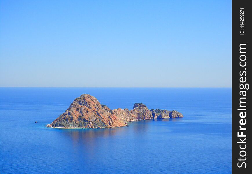 A lonely little island, a mountain in a blue ocean. Beautiful blue sky.