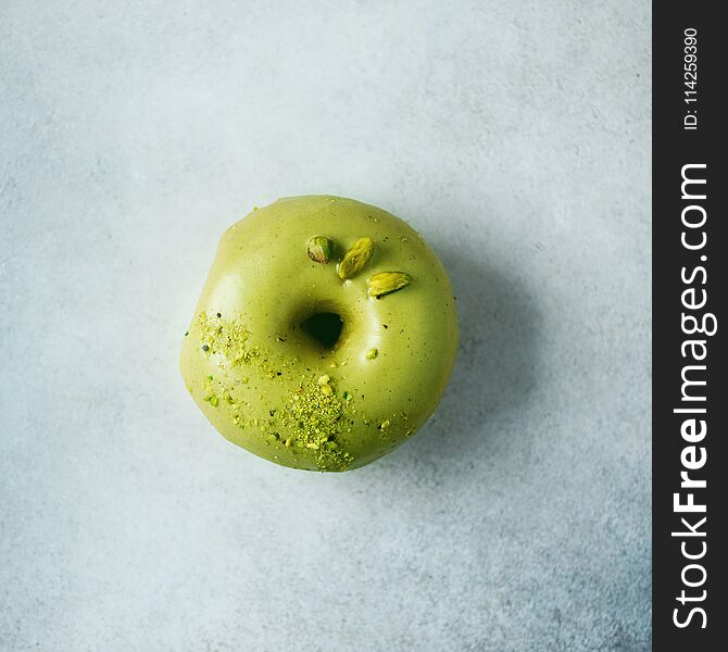 Sweet doughnut with green glaze and pistachio on grey background. Tasty donut on pastel concrete texture, copy space, top view.