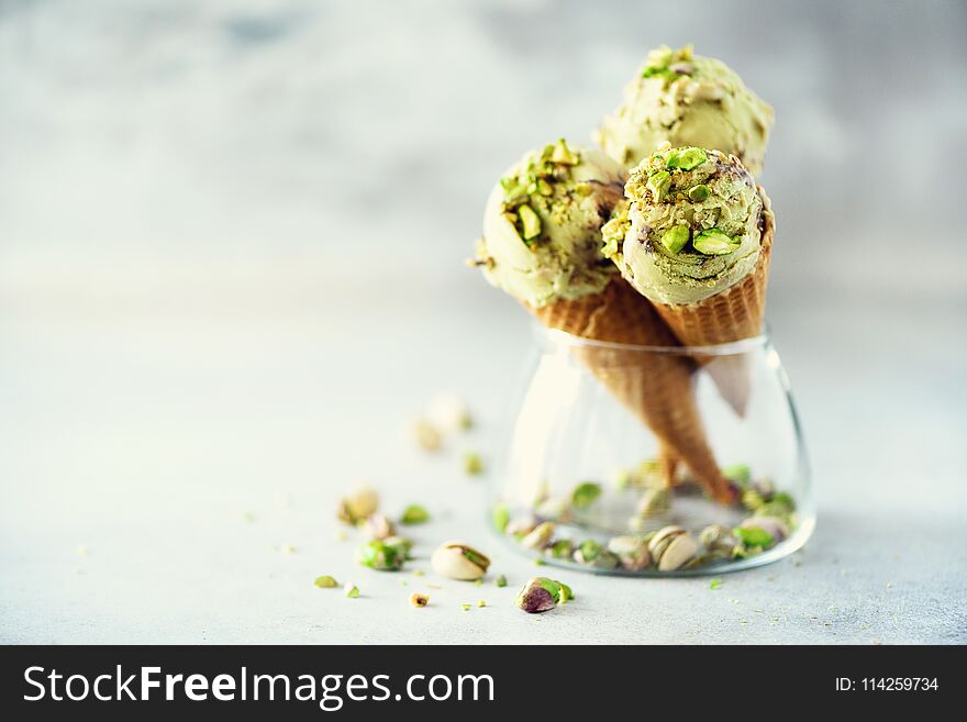 Green ice cream in waffle cone with chocolate and pistachio nuts on grey stone background. Summer food concept, copy