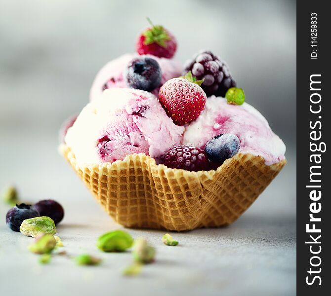 Pink ice cream with berries, strawberries, blueberries, raspberries, pistachios in waffle basket. Summer food concept, copy space. Healthy gluten free fruit ice-cream.