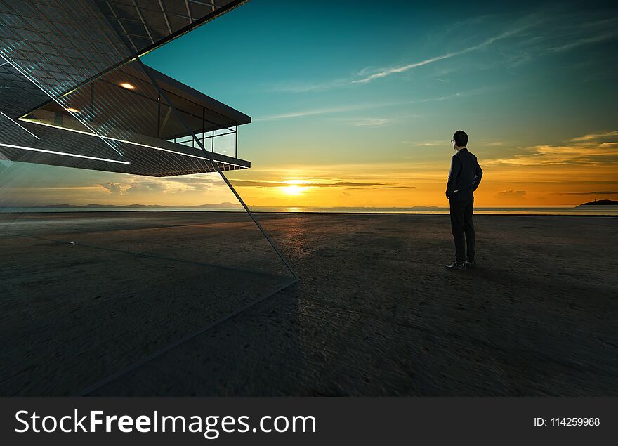 Businessman looks at sunrise thoughtfully with steel and glass facade modern building background .