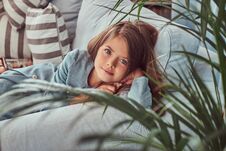 Portrait Of A Cute Little Girl With Long Brown Hair And Piercing Glance, Looking At A Camera, Lying On A Sofa At Home Stock Photos