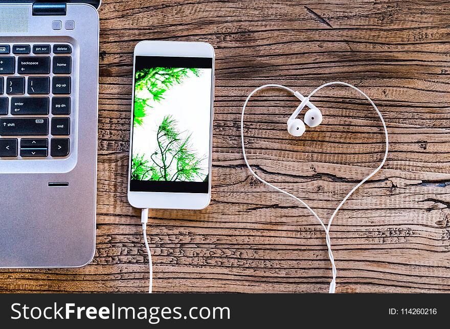 Smartphone with white heart shape earphone and computer laptop on working table flat lay composition top view with copy space