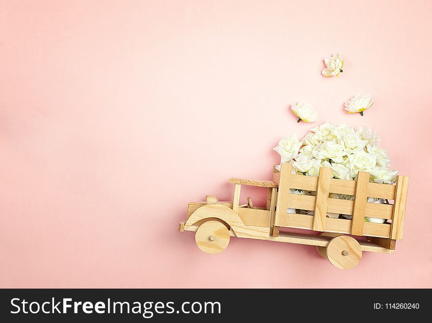 Wooden toy truck with white roses flowers in the back on pink background. Space for text. Festive greeting concept