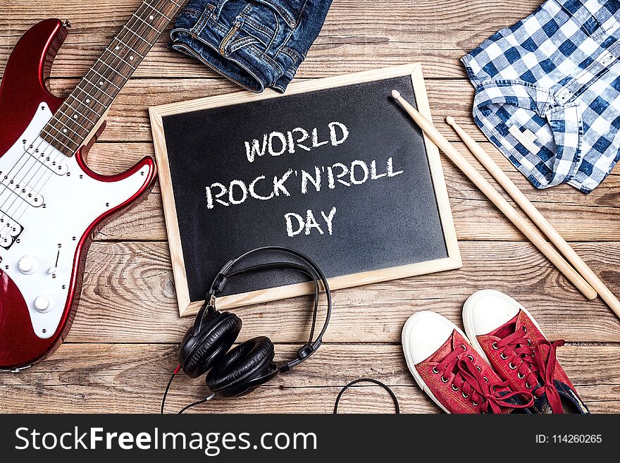 World Rock`n`Roll Day background with blackboard, music equipment, clothes and footwear on wooden table. April 13th World Rock`n`Roll Day.