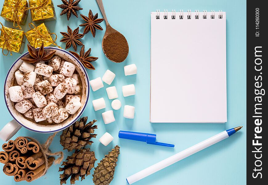 Hot drink with marshmallow and and notebook on blue background