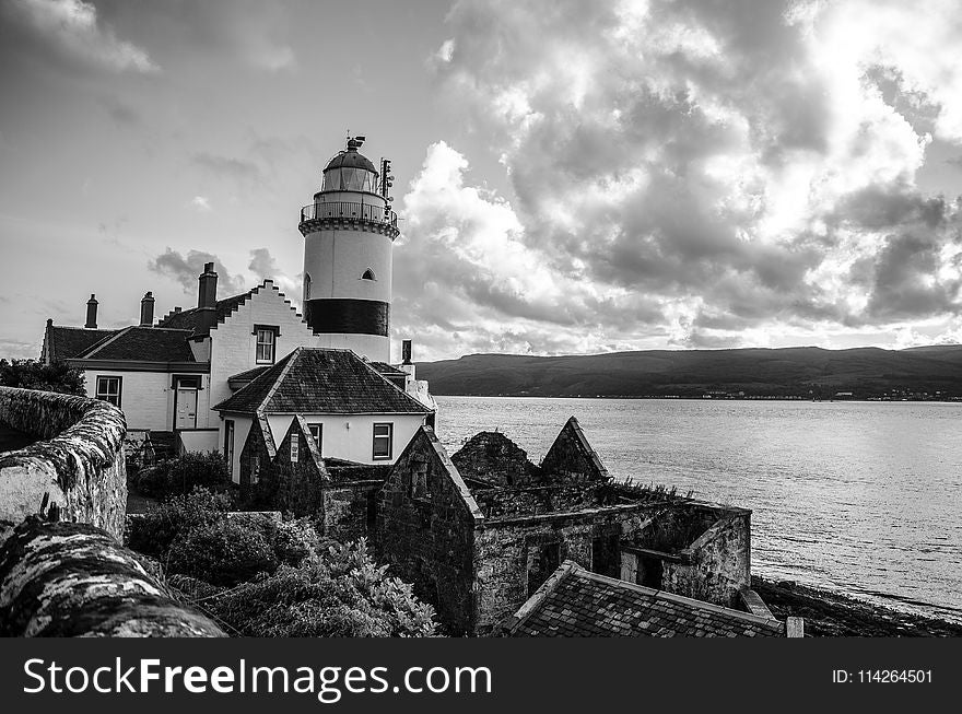 Grayscale Photo of Lighthouse on Rocky Cliff