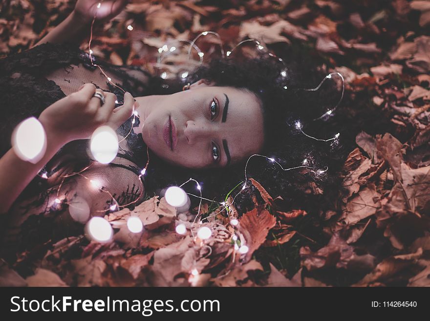 Woman Lying on Dried Leaves Holding String Lights