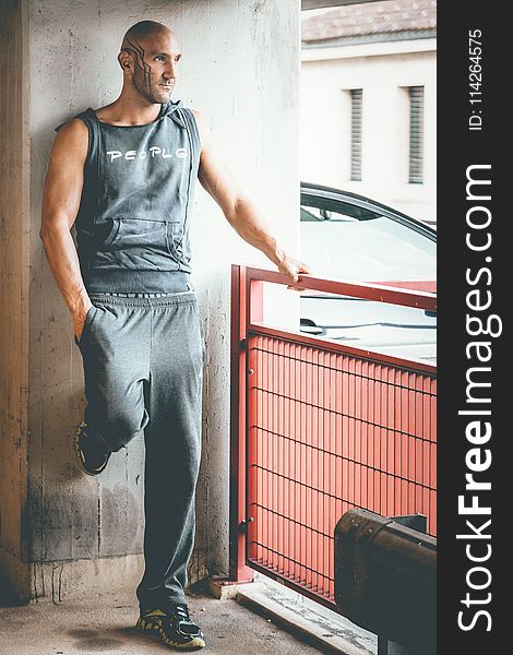 Man Wearing Gray Tank Top and Track Pants Leaning on Wall