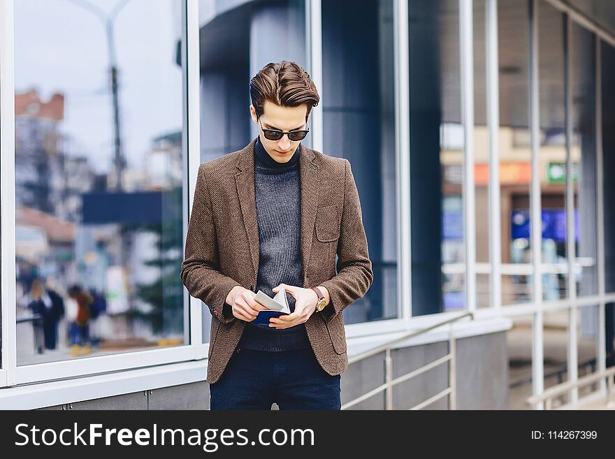 stylish attractive guy in jacket with passport and tickets outside