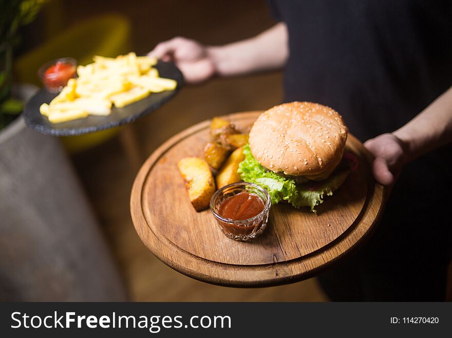 Waiter holds fresh hot burger with potatoes in restaurant. Waiter holds fresh hot burger with potatoes in restaurant