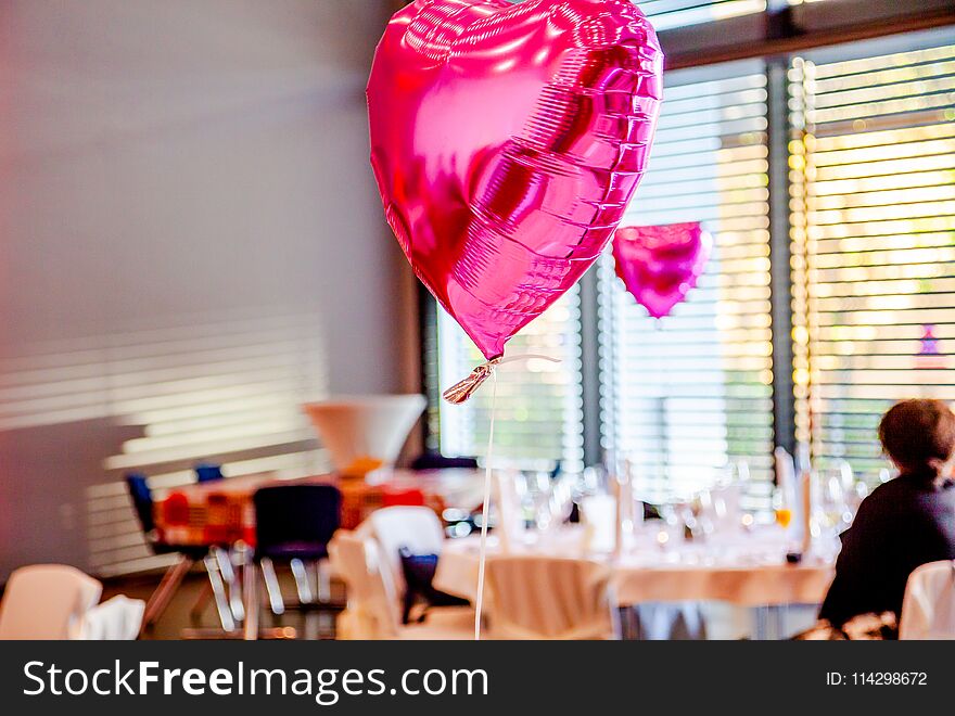 Pink festive balloons shape of heart with the party guests in the background.