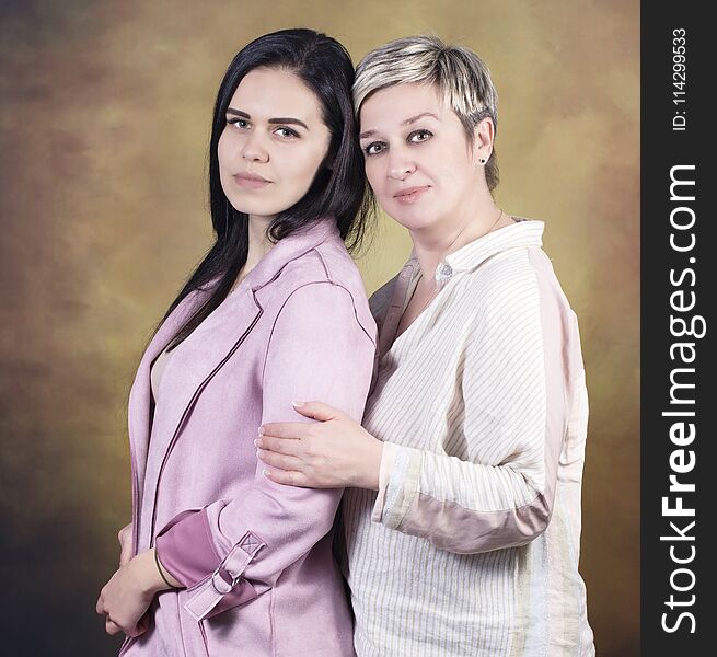 Portrait of Mother with her daughter side by side looking at the camera, on Yellow Background, closeup.