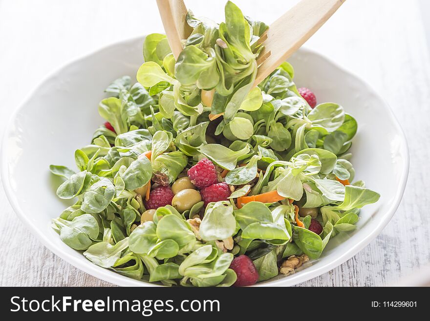 Salad of canons, raspberries, raisins, olives, nuts, carrots and pips. Wooden spoon and fork. Salad of canons, raspberries, raisins, olives, nuts, carrots and pips. Wooden spoon and fork.