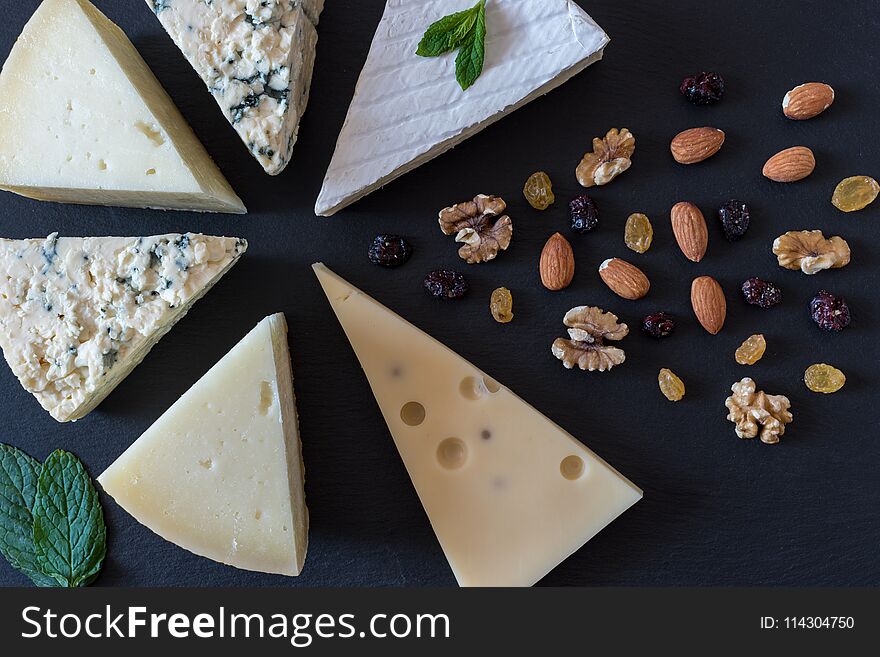 Different kinds of cheeses on black stone board with nuts