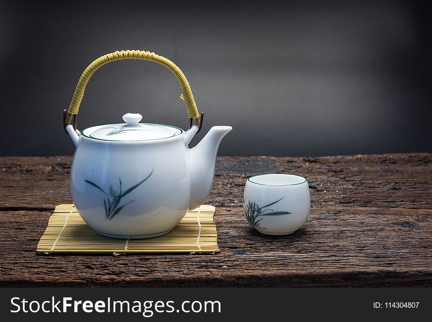 Hot tea pot on bamboo mat with cup on wooden table