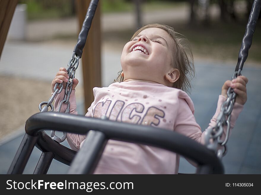 Enjoy the little girl from riding on a swing. The child is having fun, laughing, enjoying the fun games on the playground. Enjoy the little girl from riding on a swing. The child is having fun, laughing, enjoying the fun games on the playground