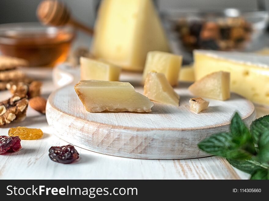 Fresh Greek cheese graviera and a slice on white wooden board with nuts, honey and herbs.