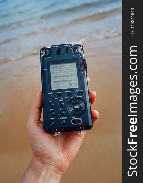 Portable audio recorder in hand recording ambient sounds of sea, closeup view