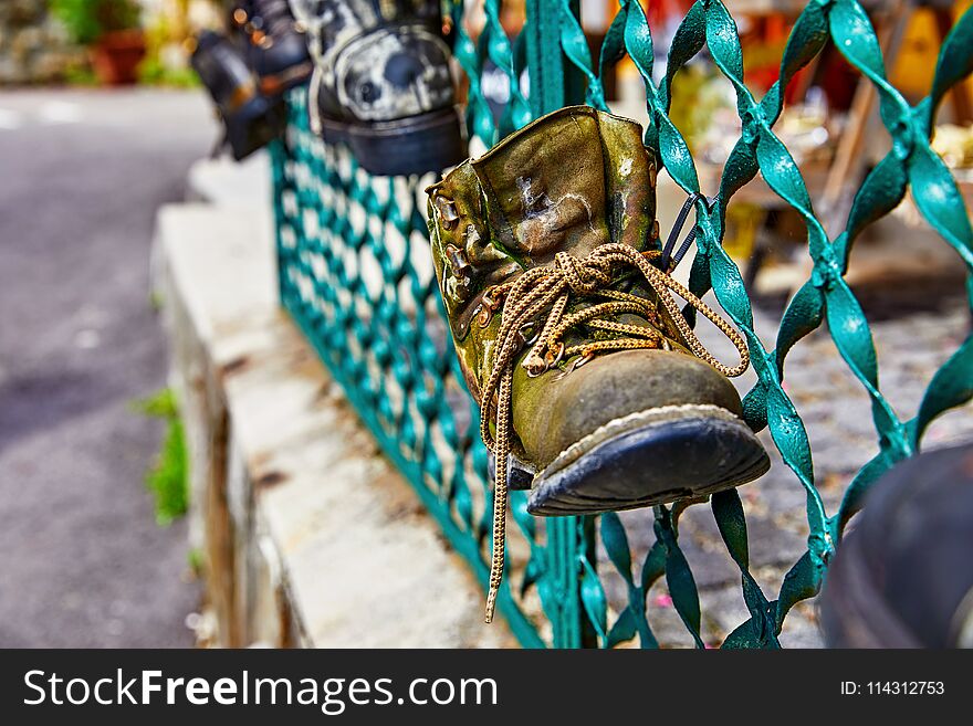 Old battered boot with lace rope used as decoration for shabby metal fence. Old battered boot with lace rope used as decoration for shabby metal fence.