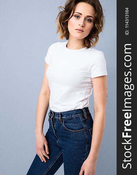 Portrait of stylish young girl in basic white t-shirt and high waisted blue jeans posing in studio on grey background