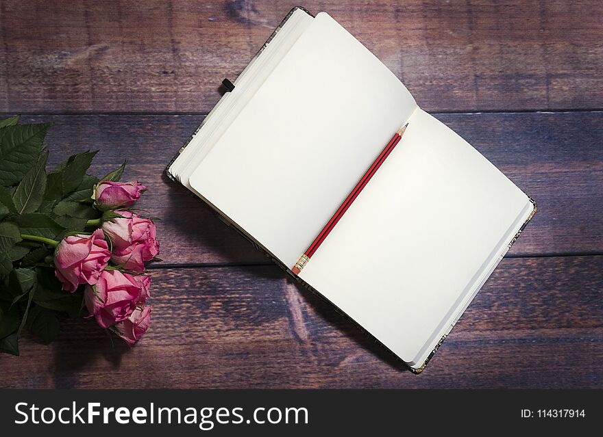 Top view of blank sheet of notebook and red and pink roses flowers on rustic brown wooden table. Copy space.