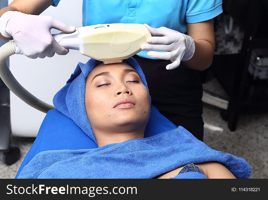 Treatment on Asian Woman as patient to make skin smooth bright and cure acne with medical beauty device instrument cold process on face in hospital clinic with acne wart. Treatment on Asian Woman as patient to make skin smooth bright and cure acne with medical beauty device instrument cold process on face in hospital clinic with acne wart