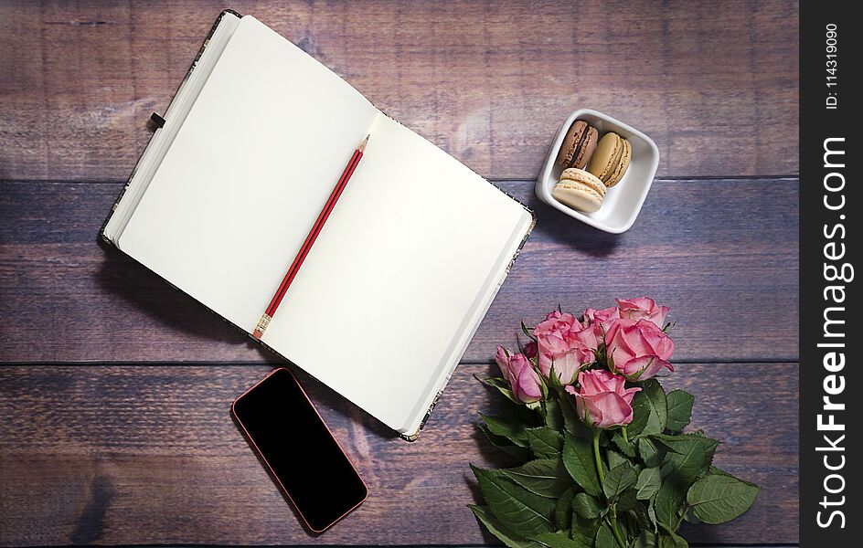 Flat lay, top view office table desk. feminine desk workspace with roses, diary, phone. Copy space. Top view of blank sheet of notebook and red and pink roses flowers on rustic brown wooden table. Copy space.