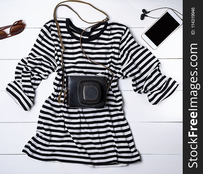 White cotton shirt in black stripes and an old vintage camera in a leather case, next is a white smartphone with black headphones