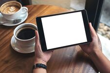 Hands Holding Black Tablet Pc With White Blank Screen And Coffee Cups On Table Royalty Free Stock Image