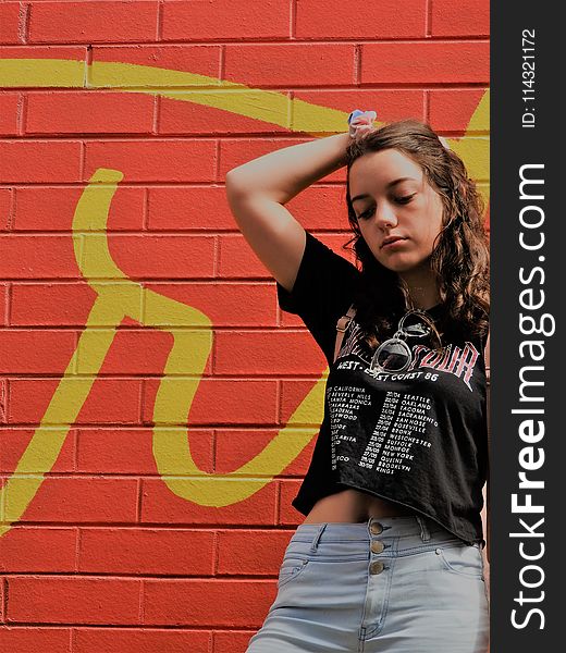 Woman In Black Shirt And Blue Bottoms Standing Near Red Wall