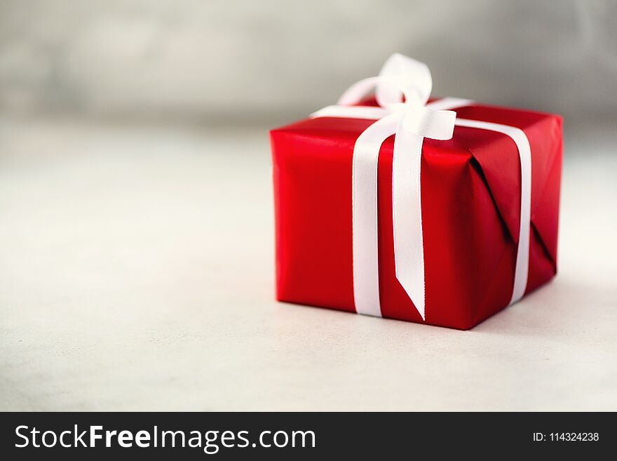 Red gift box on grey concrete background, copy space. Christmas, new year, birthday party, valentine`s day, mother`s and