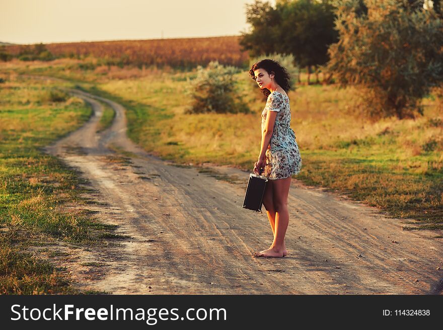 Young woman on country road with suitcase