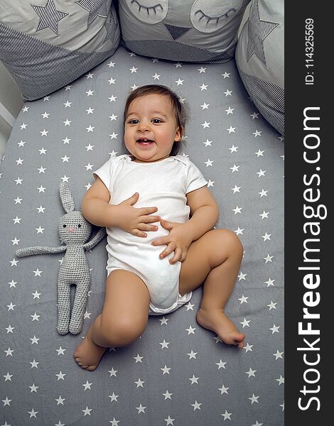 One year old baby boy lying in a round bed with a knitted rabbit toy