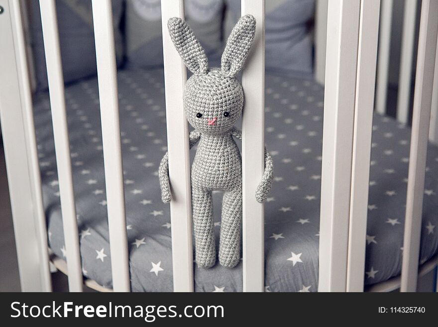 Grey knitted rabbit sitting behind the partitions