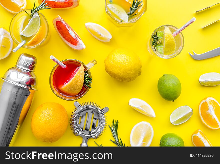 Mix exotic fruit cocktail with alcohol. Shaker and strainer near citrus fruits and glass with cocktail on yellow background top view.