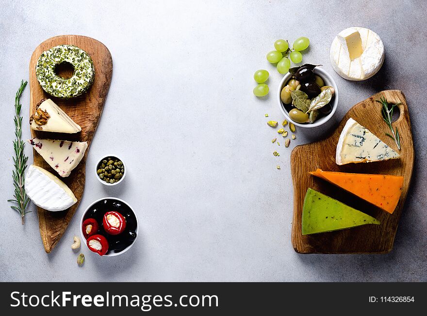 Assortment of hard, semi-soft and soft cheeses with olives, grissini bread sticks, capers, grape, on grey concrete backgound. Top view, copy space, flat lay. Cheese selection appetizer plate