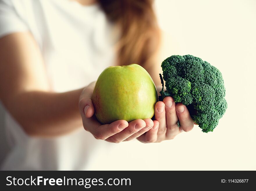 Woman in white T-shirt holding geen apple and broccoli in her hands. Copy space. Clean detox eating, vegetarian, vegan, raw concept.