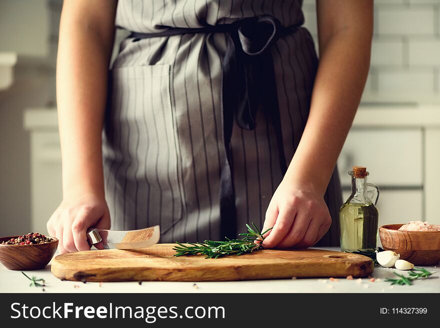 Woman hands cutting fresh green rosemary on wood chopping board in white kitchen, interior. Copy space. Homemade food