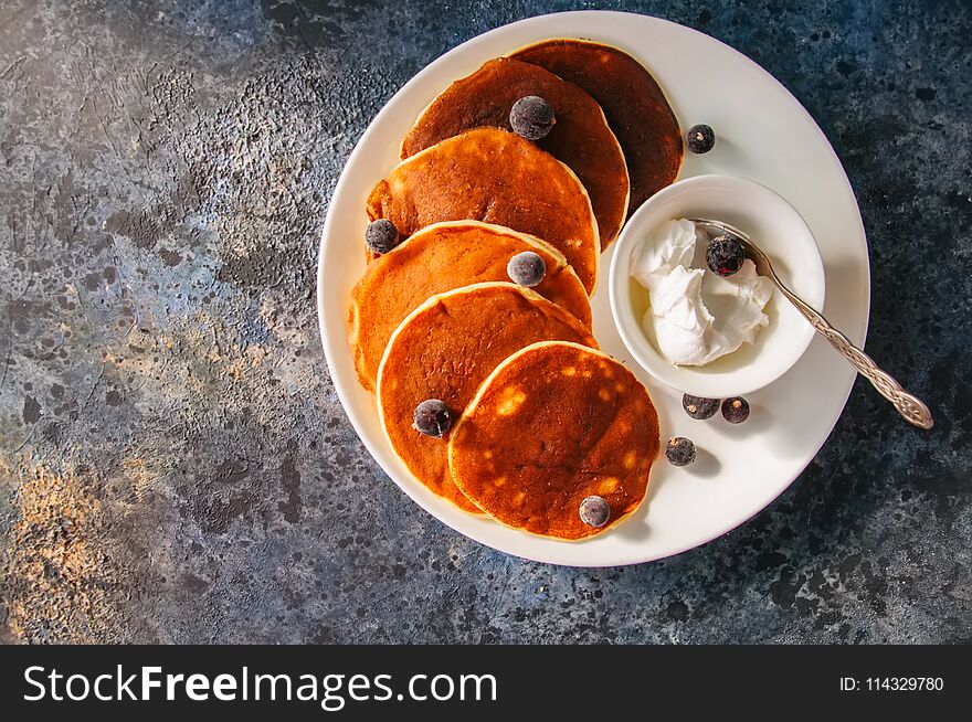 Cottage cheese pancakes with sour cream and berries on a white plate on a blue stone background.
