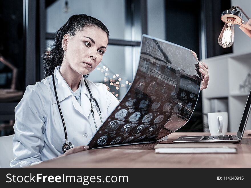 First results. Serious busy concentrated medic sitting in the her cabinet holding and overlooking x-ray scan. First results. Serious busy concentrated medic sitting in the her cabinet holding and overlooking x-ray scan.