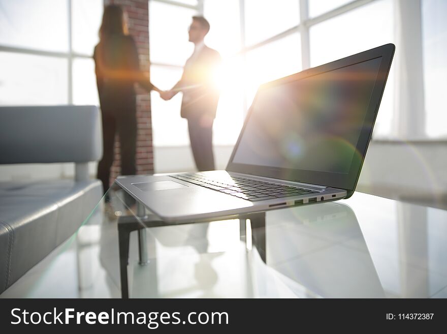 Laptop computer with folder on desk,two businesspeople standing in the background. Laptop computer with folder on desk,two businesspeople standing in the background